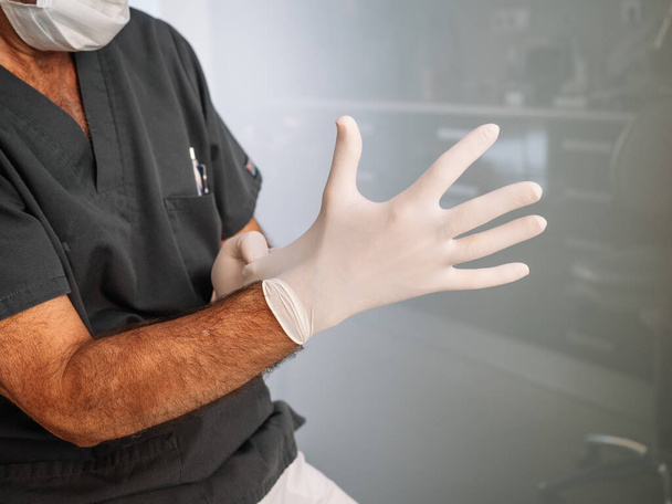 Доктор одягає латексні рукавички перед тим, як продовжувати виконувати свою роботу
 - Фото, зображення