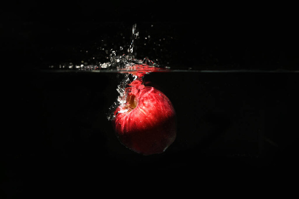 Manzanas rojas dulces caen al agua con un chapoteo y burbujas de aire sobre el fondo negro. - Foto, Imagen