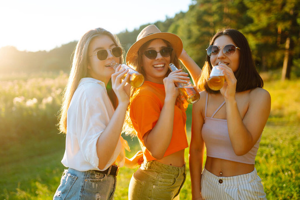 Three young woman is resting at picnic. Girlfriends  enjoy sunny day on beautiful green meadow. Vacation, picnic, friendship or holliday concept. - Foto, Imagem