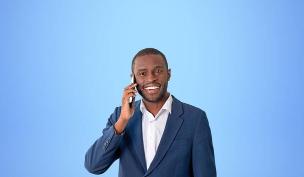 Uomo d'affari felice che parla sullo smartphone, ritratto sorridente su sfondo blu spazio copia. Concetto di successo, buone notizie, carriera e sviluppo - Foto, immagini