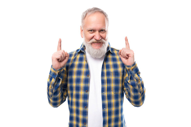 gepflegter erwachsener grauhaariger Mann mit Bart im Hemd zeigt mit dem Finger auf einen weißen Hintergrund mit Kopierraum. - Foto, Bild