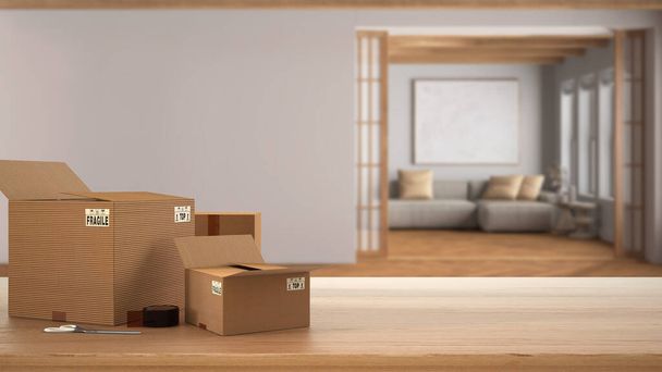 Table, bureau ou étagère en bois avec pile de boîtes en carton sur une vue floue du salon japandi dans un style minimal, design d'intérieur, concept de maison mobile avec espace de copie - Photo, image