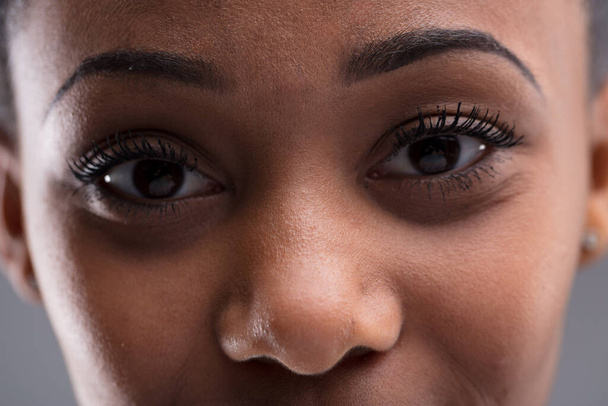 Close-up portrait of a young woman of color's eyes. Minimal depth of field, deer-like nose and eyes near. Mirror of the soul or checking for skin blemishes? Perfect eyebrows - Фото, зображення
