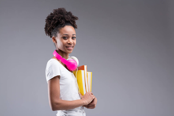 Uma menina estudiosa com fones de ouvido rosa e livros coloridos compartilha seus pensamentos. A educação custa dinheiro e esforço, mas promete um futuro melhor. Comprometida com o seu bem-estar - Foto, Imagem