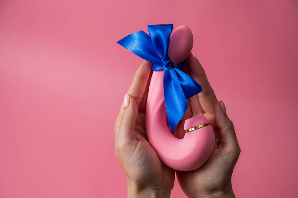 Woman holding curved dildo with blue ribbon on pink background. Copy space - Foto, immagini