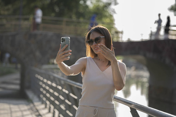 Backlit summer portrait of a young brunette woman in sunglasses. A woman sends an air kiss to an interlocutor on a video call. High quality photo - Fotografie, Obrázek