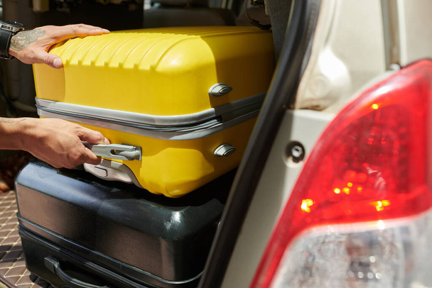Closeup image of man taking luggage out of car trunk - Photo, Image