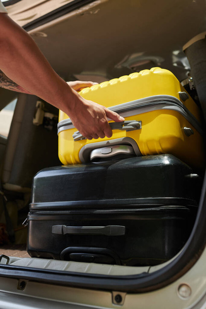 Imagen de primer plano del conductor del traslado al aeropuerto sacando las maletas del maletero del coche - Foto, imagen