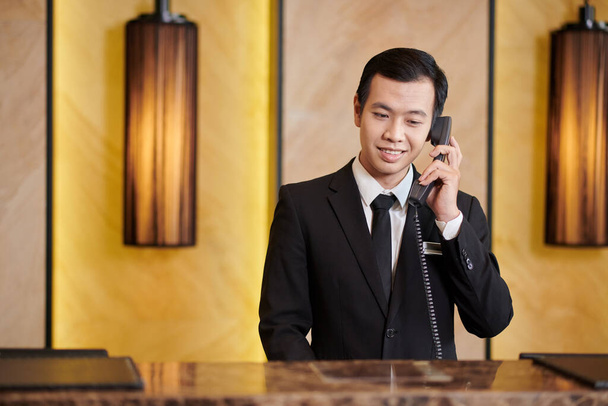 エレガントなスーツで笑顔ベトナムのホテルの受付電話を作る - 写真・画像