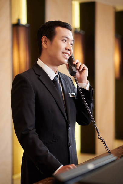 Luxurious hotel receptionist in elegant suit answering phone call - 写真・画像