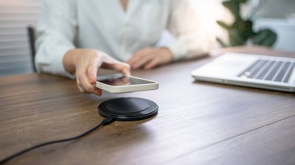 Charging mobile phone battery with wireless charging device in the table. Smartphone charging on a charging pad. Mobile phone near wireless charger Modern lifestyle technology  - Fotoğraf, Görsel