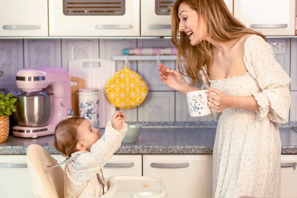 Young mom talking with her baby girl in the kitchen - Fotografie, Obrázek