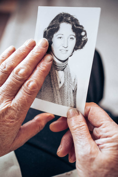 CIRCA 1970: Elderly woman hands holding vintage, black and white photo of the young woman. Passing of time concept - Foto, imagen