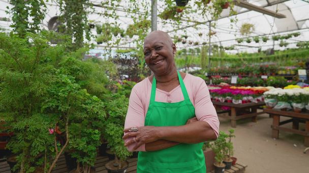 A joyful black female worker with arms crossed looking at camera smiling inside flower shop. Local business store concept - Photo, Image