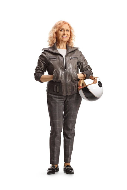 Full length portrait of a stylish mature woman in a leather jacket carrying a helmet isolated on white background - Zdjęcie, obraz