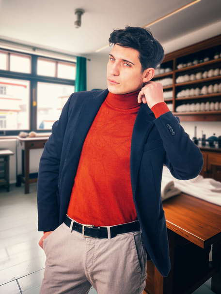 Pensive attractive man with black hair in stylish outfit standing in atelier and touching blazer - 写真・画像