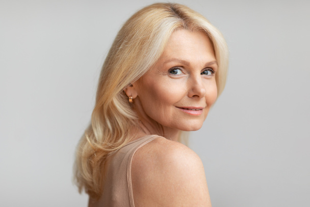 Portrait of beautiful mature lady with bare shoulders posing over light grey studio background, good-looking aged woman with natural makeup looking at camera - Φωτογραφία, εικόνα