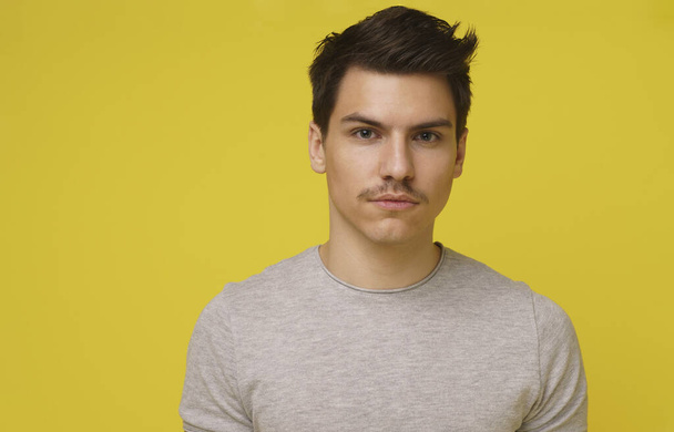 Head shot of young charming man 20s with mustache looking at the camera isolated on yellow background. - Photo, Image
