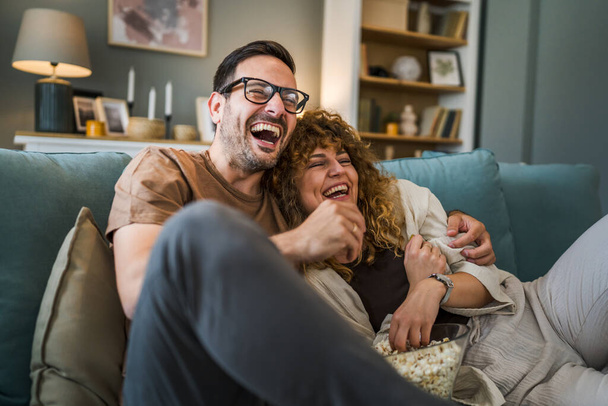Couple man and woman caucasian husband and wife or boyfriend and girlfriend sit on the sofa bed at home watch tv movie series with bowl of popcorn happy smile bonding love family concept copy space - Foto, imagen