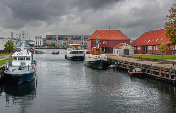Copenhagen, Denmark - September 14, 2010: Historic red military buildings along canal in Christianshavn under gray cloudscape. Admiral hotel on other side of harbor. Small vessels docked - Foto, imagen