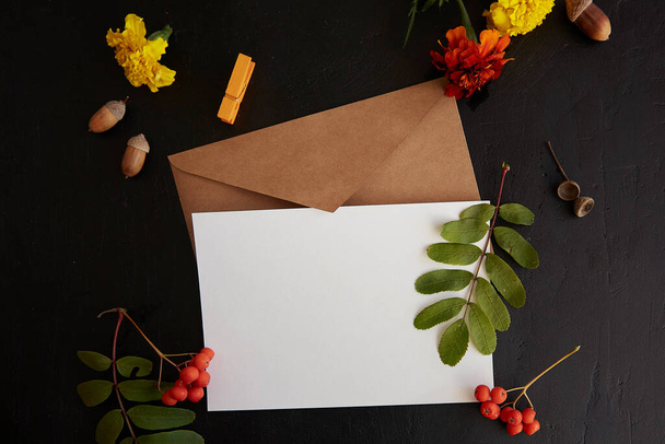Elaboración de sobres con postal vacía, tarjeta de papelería se burlan de entre las flores estéticas de otoño y hojas de cerca. Fondo atmosférico. - Foto, imagen