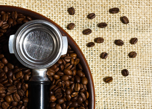 Habas de café Arábica seleccionadas. Un cono de café y granos de café se encuentran en un plato de cerámica sobre un fondo de arpillera. - Foto, imagen
