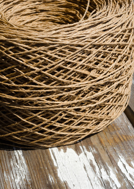 Spiedino di rafia su una vecchia tavola di legno. Un rotolo di rafia beige è pronto per essere lavorato a maglia. - Foto, immagini