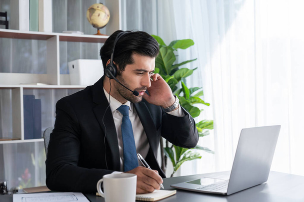 Muž operátor call centra nebo telesales zástupce sedí u svého psacího stolu nosí sluchátka a zabývá se rozhovorem s klientem poskytující zákaznickou podporu nebo prodej. horlivý - Fotografie, Obrázek
