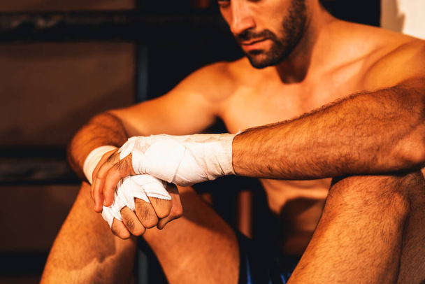 Tired and exhausted caucasian boxer removed his boxing glove and sitting, resting on the edge of the ring after intense training or fighting match. Impetus - Photo, Image