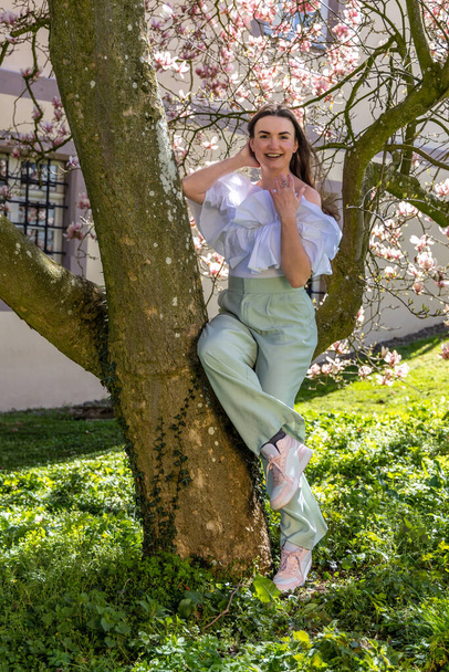 Kuva nuoresta naisesta lähellä kukkivaa magnoliaa - Valokuva, kuva