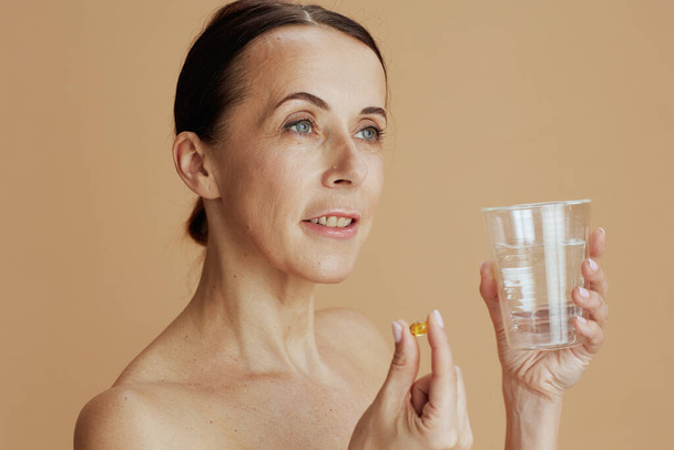 modern 40 years old woman with glass of water and pill isolated on beige. - Foto, Imagen