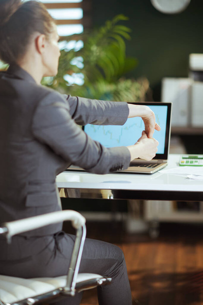 Βιώσιμος χώρος εργασίας Βλέποντας πίσω από τη σύγχρονη γυναίκα των επιχειρήσεων σε ένα γκρι κοστούμι των επιχειρήσεων σε μοντέρνο πράσινο γραφείο τεντώνει το χέρι. - Φωτογραφία, εικόνα