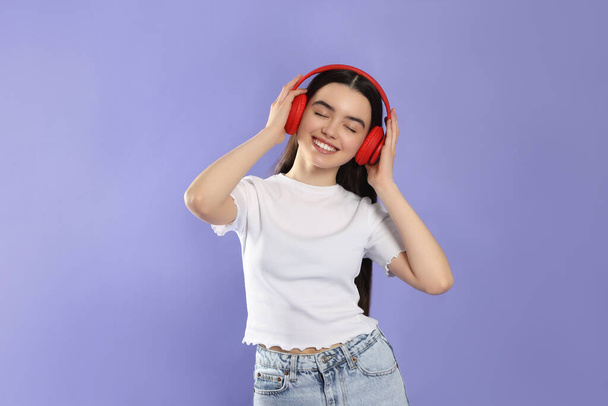 Teenage girl listening music with headphones on violet background - Foto, Imagem