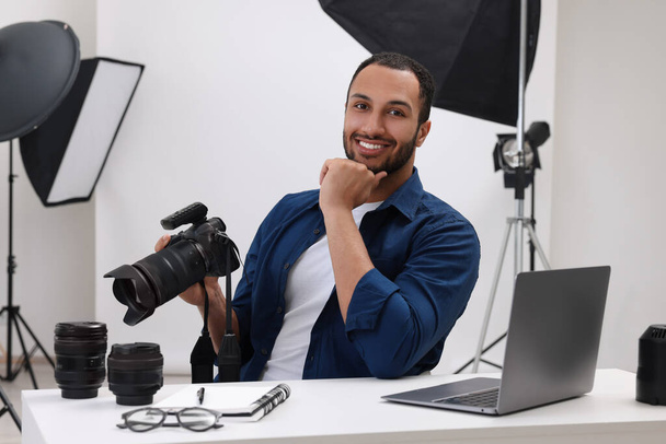 Young professional photographer with camera at table in modern photo studio - Fotó, kép
