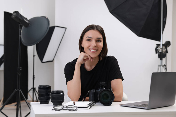 Young professional photographer with camera at table in modern photo studio - Fotó, kép