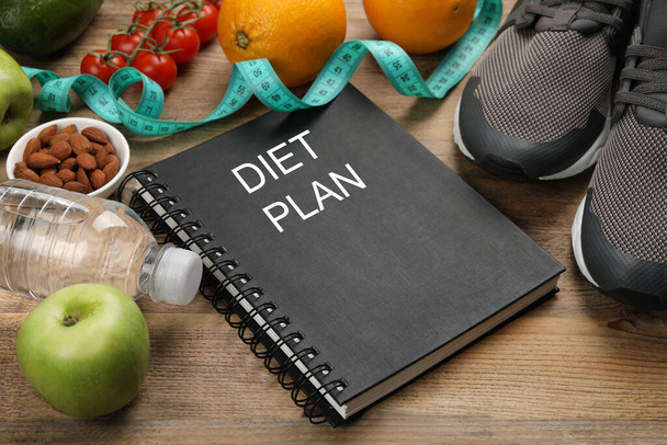 Notebook with phrase Diet Plan, sneakers and different products on wooden table - Foto, immagini