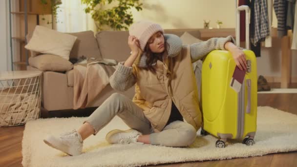 Egy csalódott fiatal nő bőröndös kalapban, útlevéllel és jegyekkel a szőnyegen ülve. Egy szomorú nő utazó boldogtalan egy sikertelen utazással. Utazási dokumentáció.Jogi követelmények. - Felvétel, videó