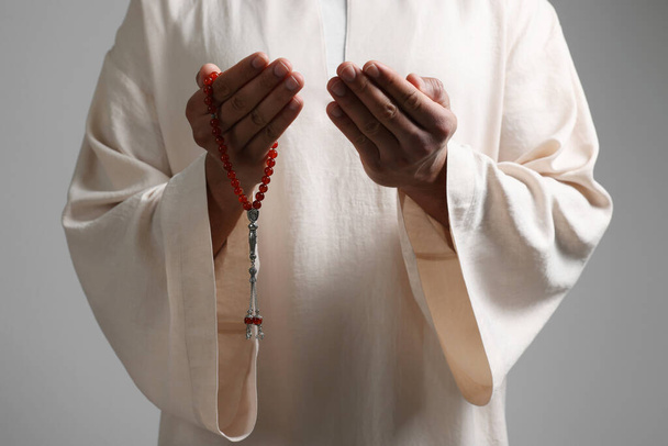 Muslim woman with misbaha praying on light grey background, closeup - 写真・画像