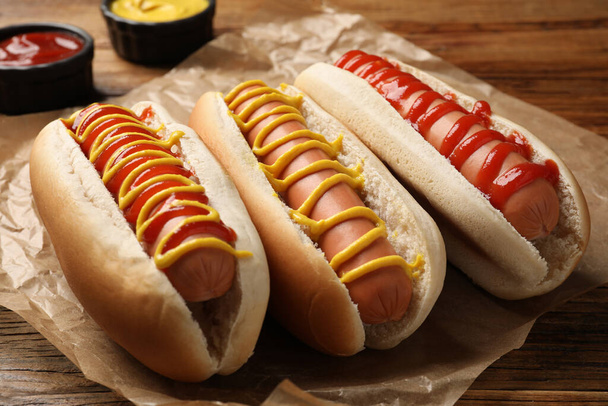 Delicious hot dogs with mustard and ketchup on wooden table, closeup - Foto, afbeelding