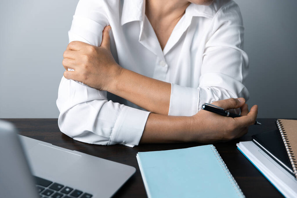 Az irodai dolgozó egy ázsiai nő, aki a laptop előtt ül. Egy üzletasszony stresszeli a testrészeit, az ujjait, a kezét. Egy női irodavezető kimerült a munkahelyén.. - Fotó, kép