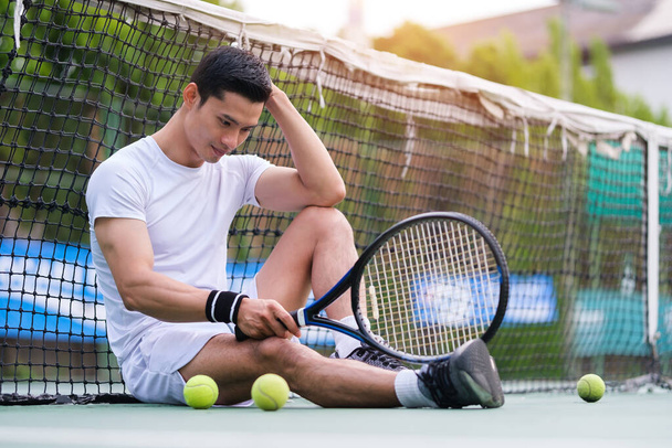 Exhausted man tennis player sitting on the court looking disappointed after practice. - Foto, Imagem