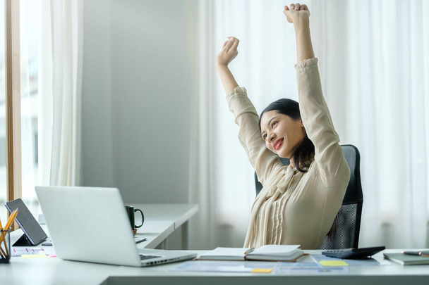 Χαρούμενη χαλαρή γυναίκα υπάλληλος κάθεται στο γραφείο τεντώνει τα χέρια της πάνω από το κεφάλι, λαμβάνοντας διάλειμμα από την εργασία. - Φωτογραφία, εικόνα