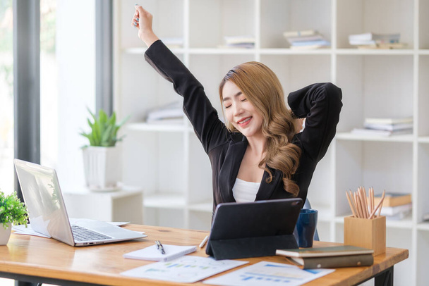 Happy female employee stretching her arms in the air, relaxing at workplace. - Foto, imagen