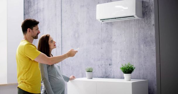 Happy Young Couple Adjusting Temperature Of Air Conditioner By Remote - Foto, imagen