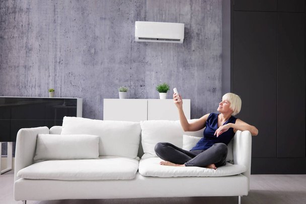 Happy Young Woman Holding Remote Control Relaxing Under The Air Conditioner - Fotoğraf, Görsel