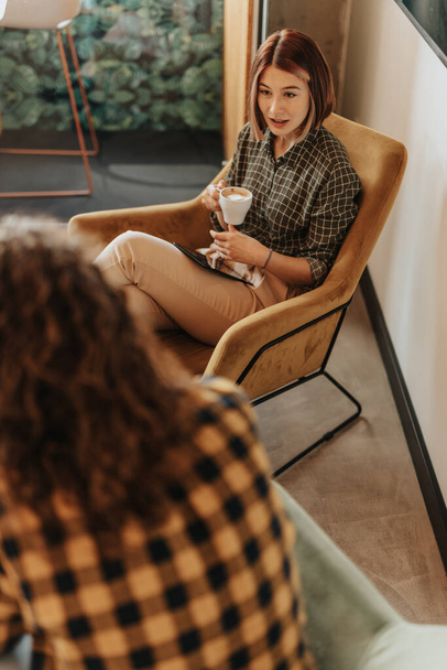 Над просмотром снимок великолепной девушки, держащей чашку кофе, разговаривающей со своим длинноволосым коллегой - Фото, изображение