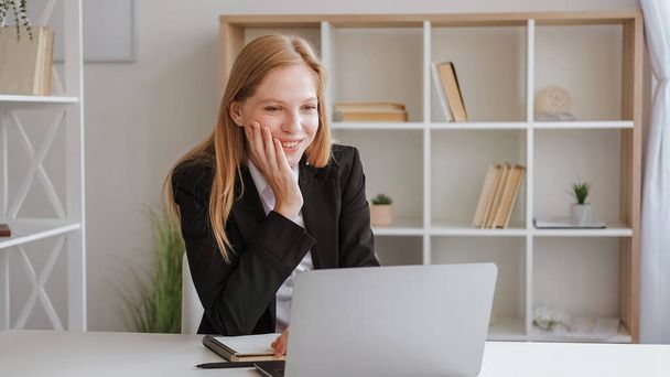 Online course. Day study. Distance learning. Happy smiling woman in business suit sitting chin on hand at desk with laptop and notes in light room. - Фото, изображение