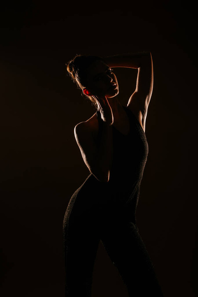Upea tyttö poseeraa studiossa. Hän koskettaa päätään ja pukeutuu mustiin kuohuviin haalareihin - Valokuva, kuva