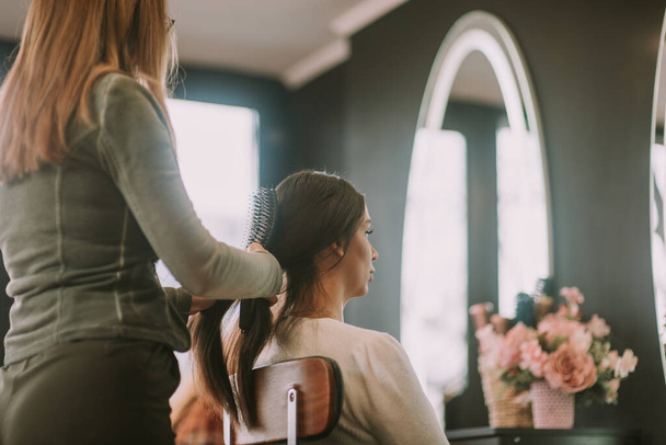 Primo piano di parrucchiere bionda spazzolare i suoi clienti capelli castani mentre si siede al salone di parrucchiere - Foto, immagini