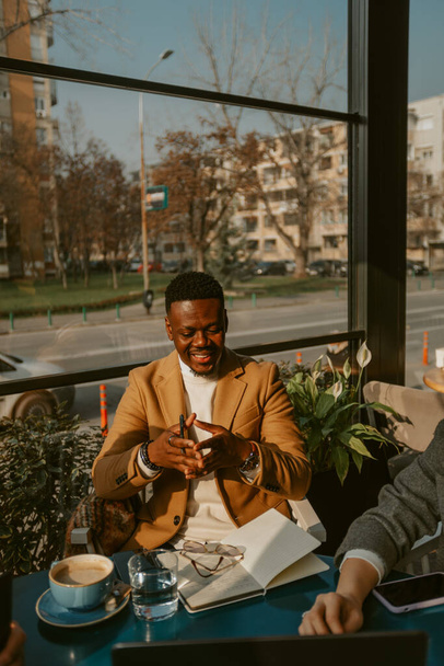 Bello uomo d'affari in ocra cappotto sorridente mentre seduto al caffè - Foto, immagini